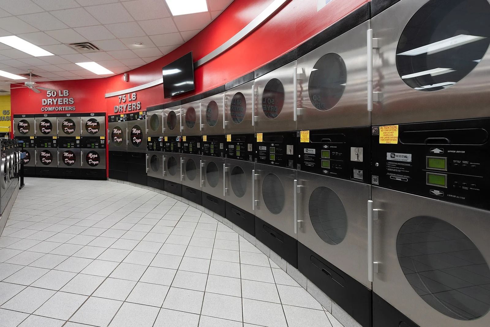 Row of stainless steel dryers in a laundromat with red and white interior.
