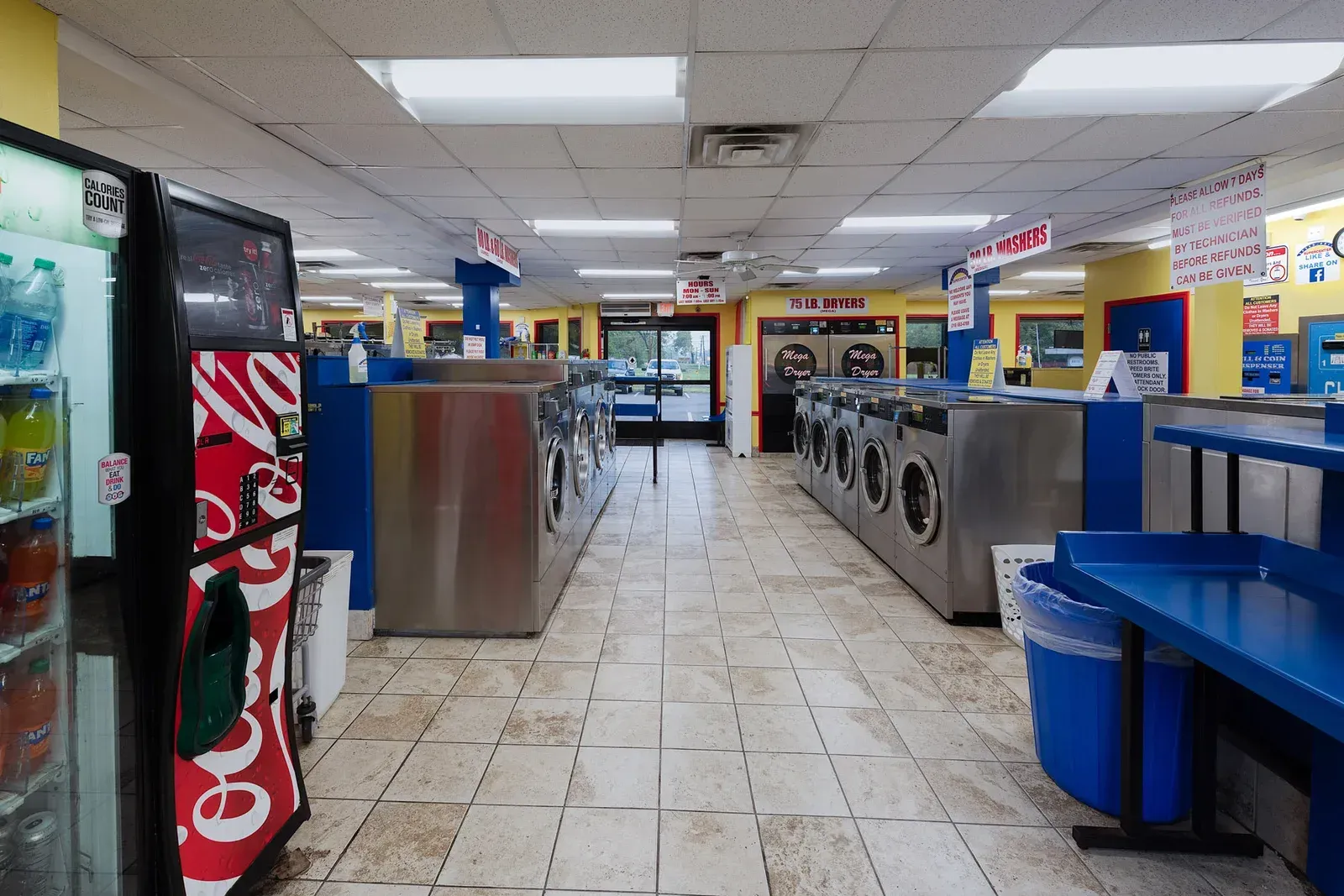 Interior of a laundromat with rows of washers and dryers, vending machines, and blue accents.