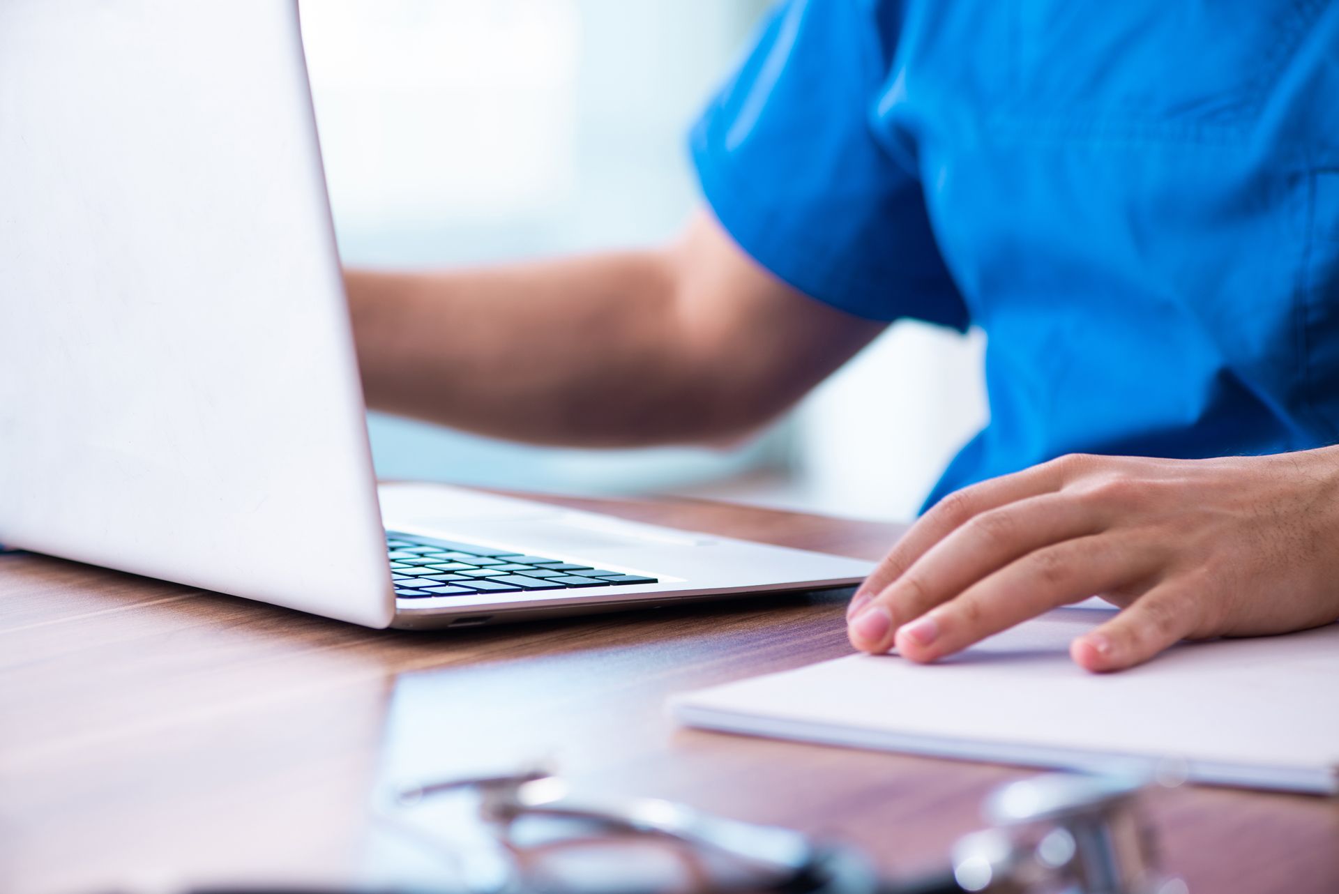 A Doctor is Typing on a Laptop Computer While Sitting at a Desk