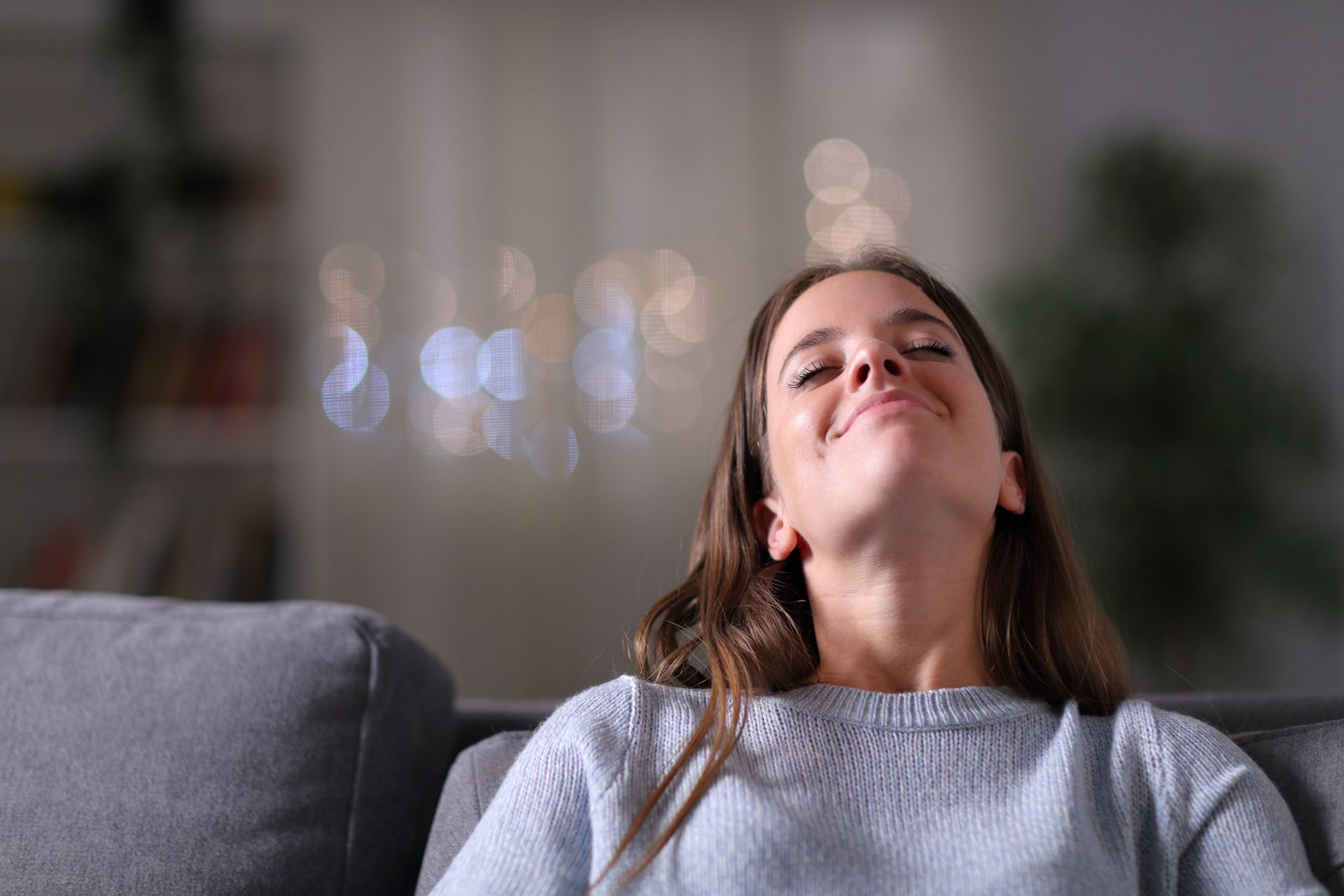 A Woman is Sitting on a Couch With Her Eyes Closed and Smiling