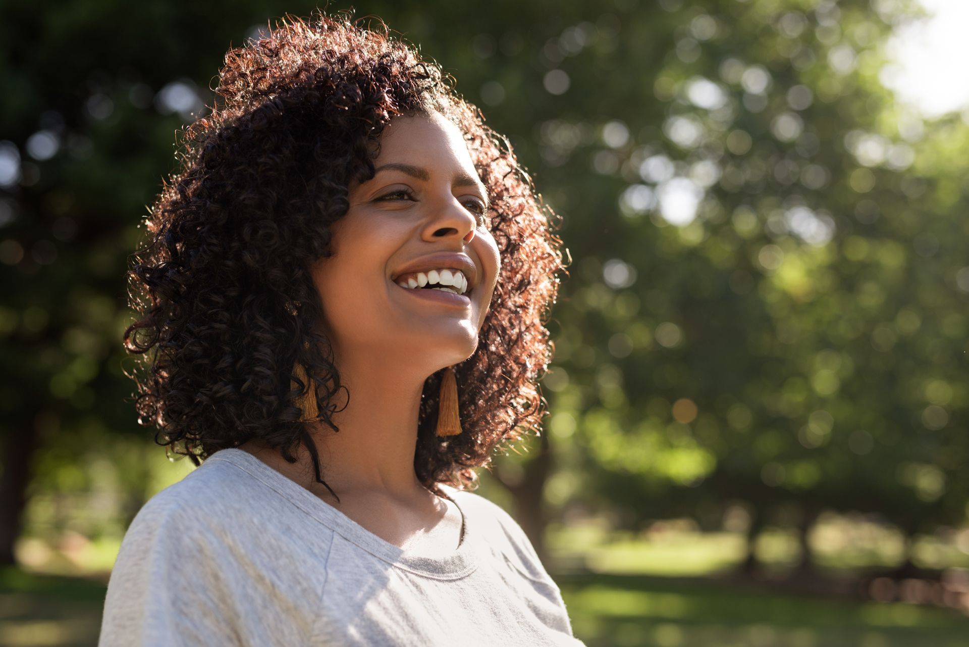 A Woman With Curly Hair is Smiling in a Park