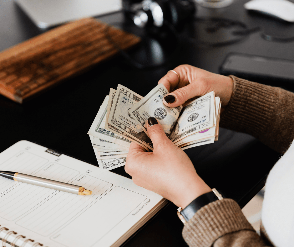 Hands counting a stack of US dollar bills over a notebook and pen. Hands counting a stack of US dollar bills over a notebook and pen.