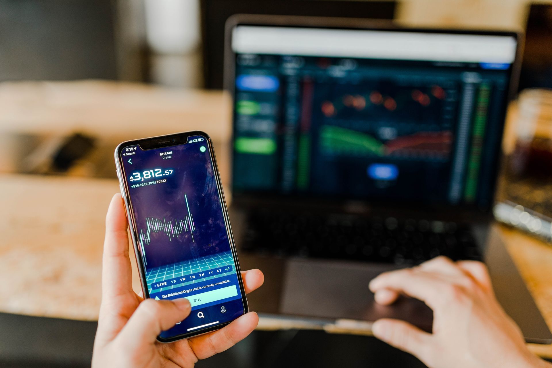 Person using a smartphone and laptop to view stock market graphs. Person using a smartphone and laptop to view stock market graphs.