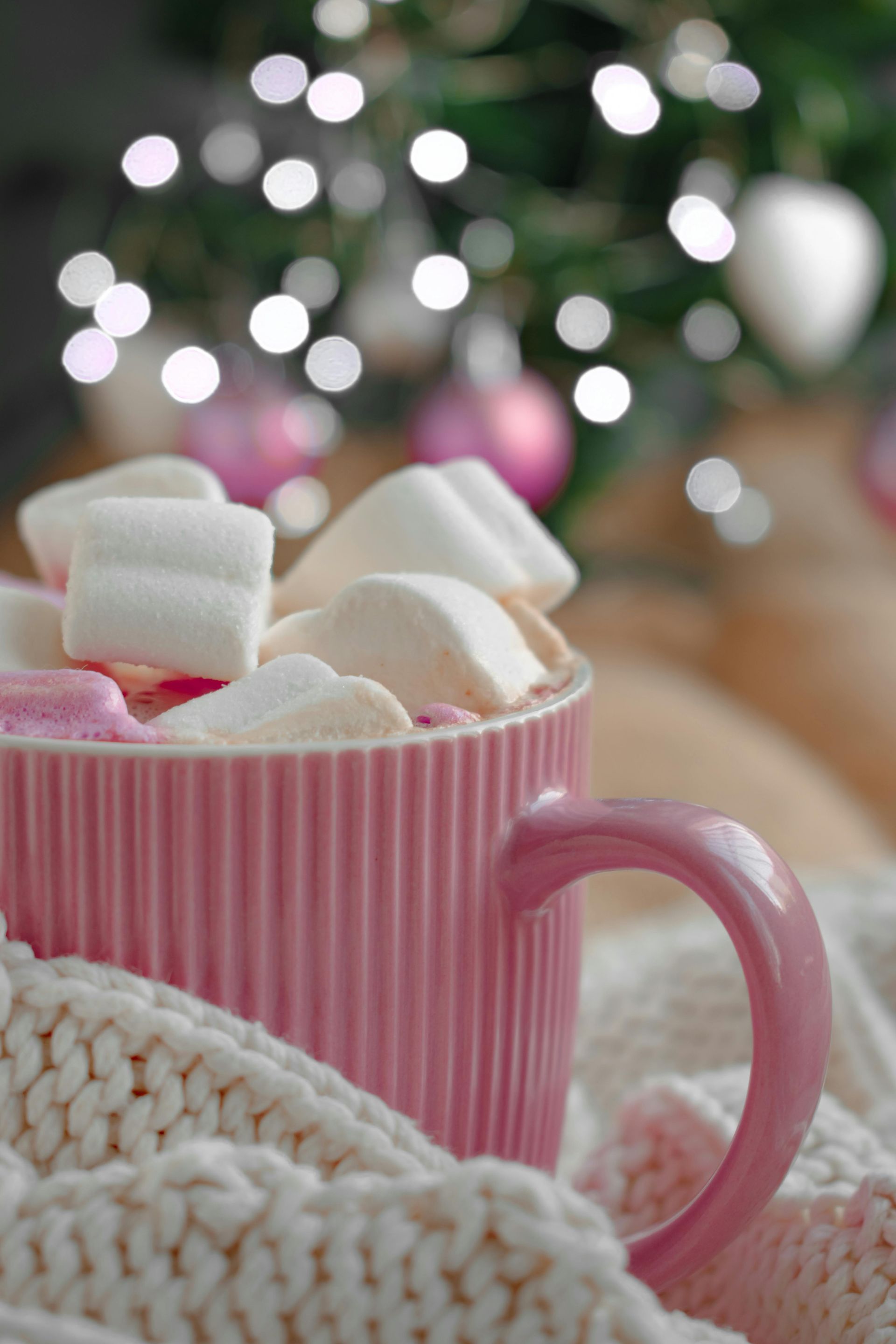 Pink mug filled with marshmallows, wrapped in a cozy cream-colored knit. Pink mug filled with marshmallows, wrapped in a cozy cream-colored knit.