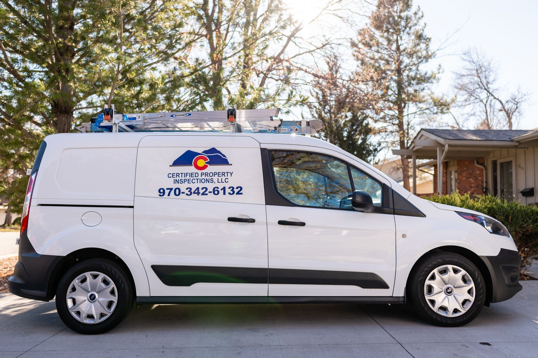 White service van with company logo and phone number parked on a street in front of a house
