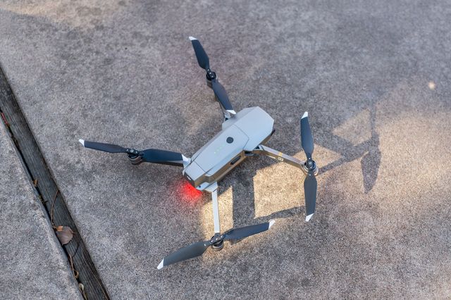 Gray quadcopter drone on concrete, red light glowing beneath it.