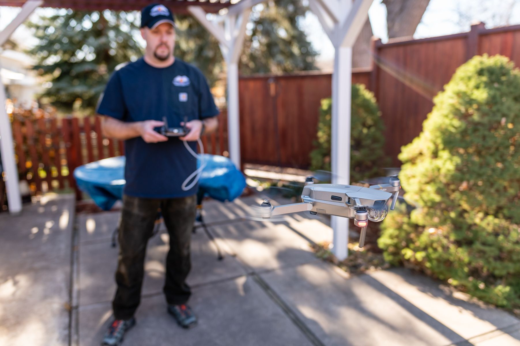 Man operating a drone controller in a backyard, with a drone flying nearby.