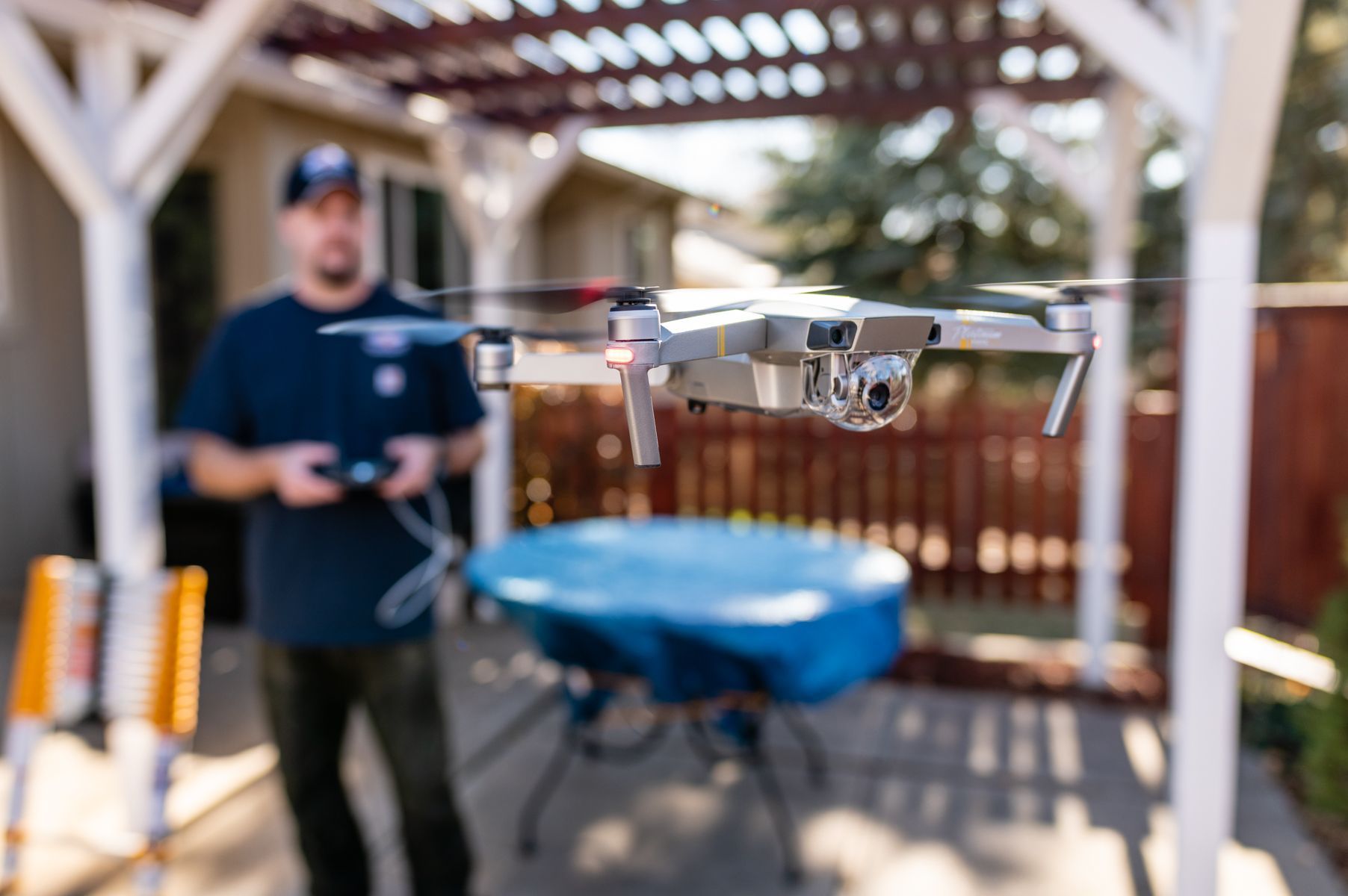 Small drone hovering outdoors near a man in a backyard patio setting