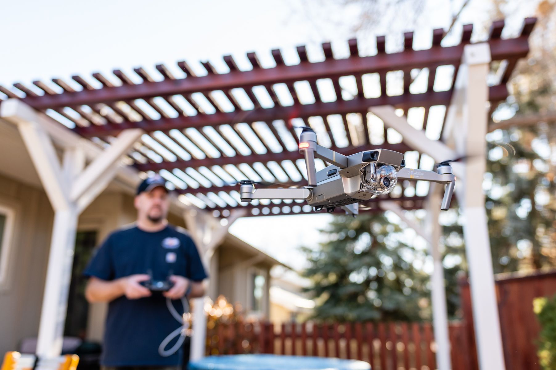 Person flying a drone under a wooden pergola in a backyard