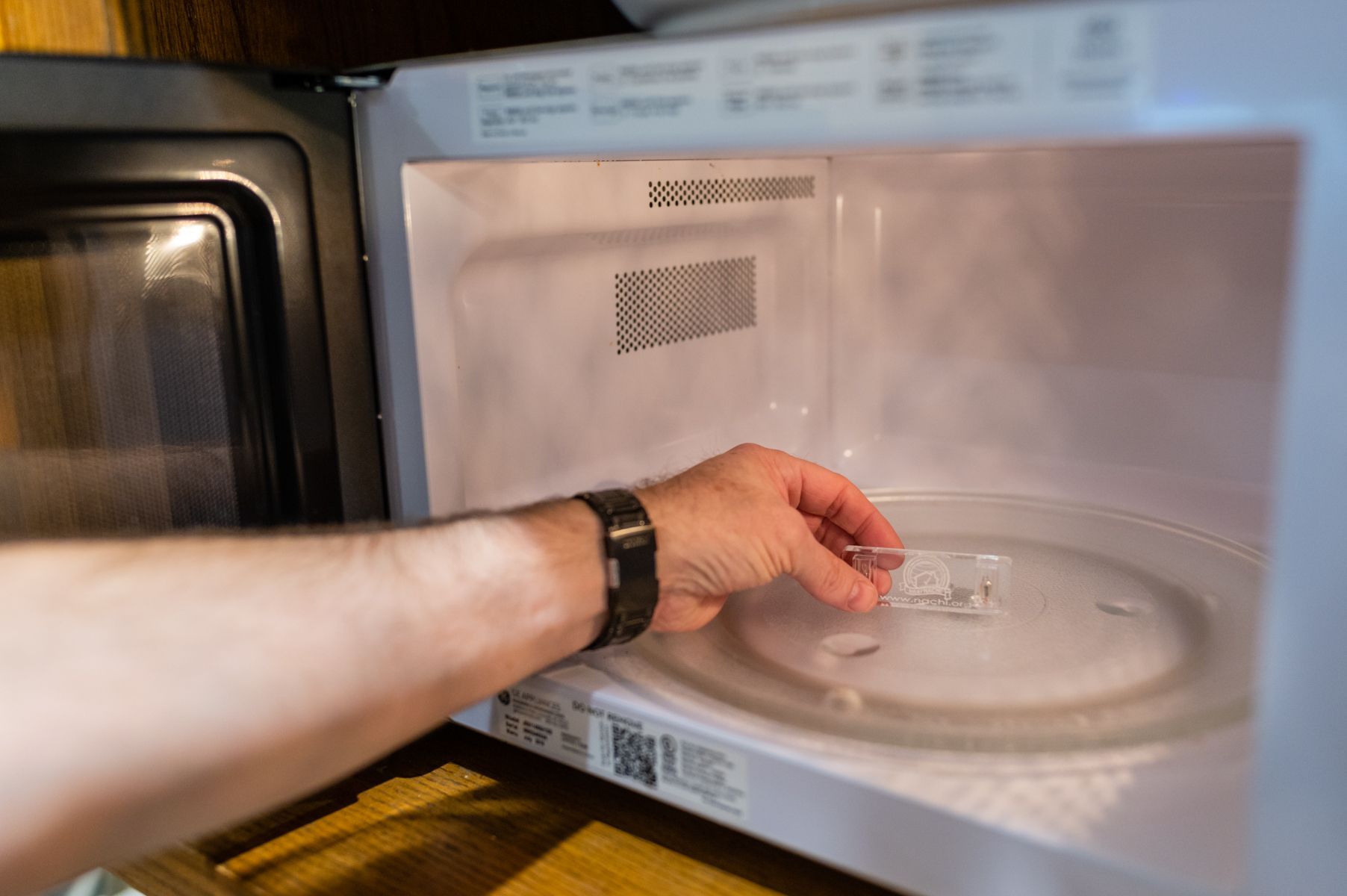 Hand placing a glass dish on a microwave turntable inside an open microwave