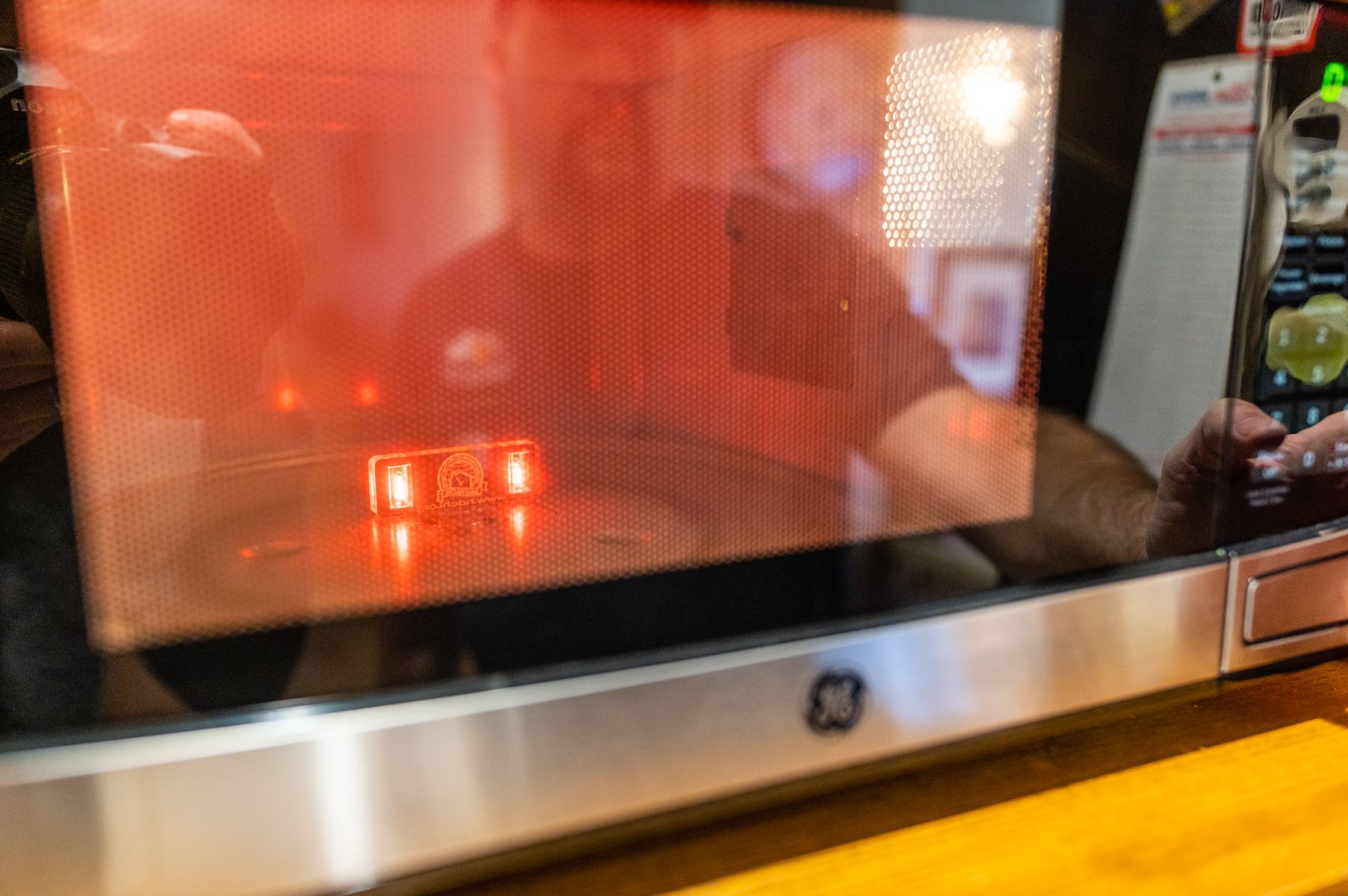 Microwave oven with lit interior and a small red-lit item inside on a kitchen counter