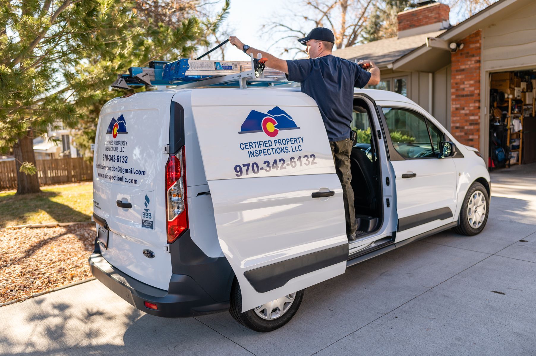 Man opening the side door of a white service van parked in a driveway outdoors