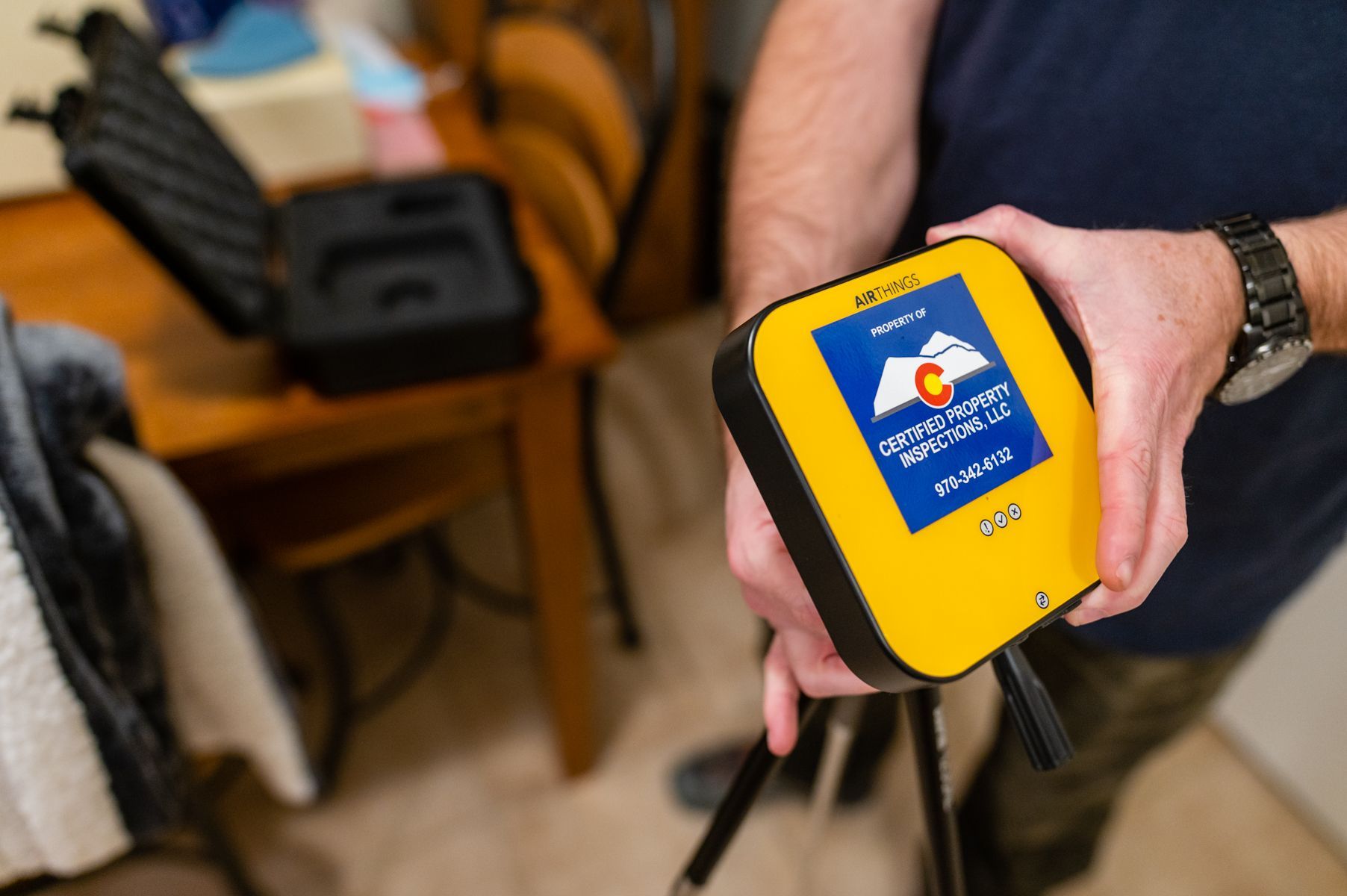 Hand holding a yellow handheld device with a blue label in a blurred indoor room