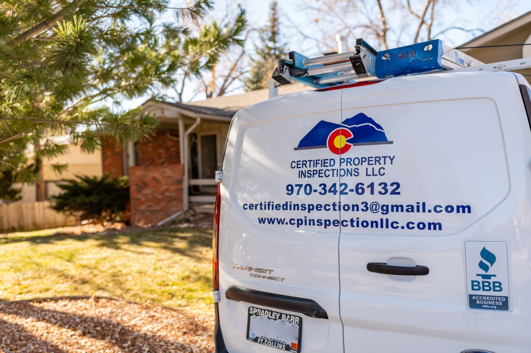 White inspection van with company logo and contact info parked in a sunny residential yard
