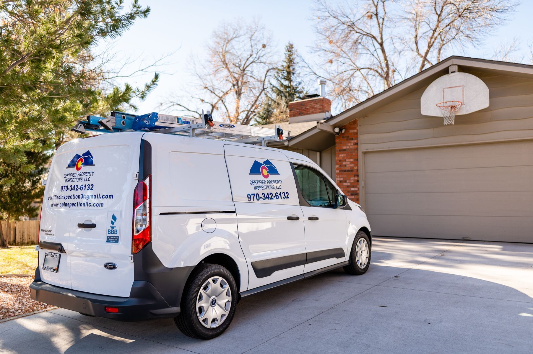 White service van parked in a driveway beside a garage with a basketball hoop.