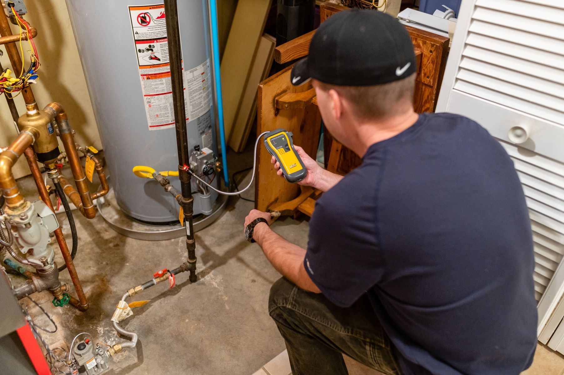 Technician using a yellow meter to inspect plumbing equipment in a utility room