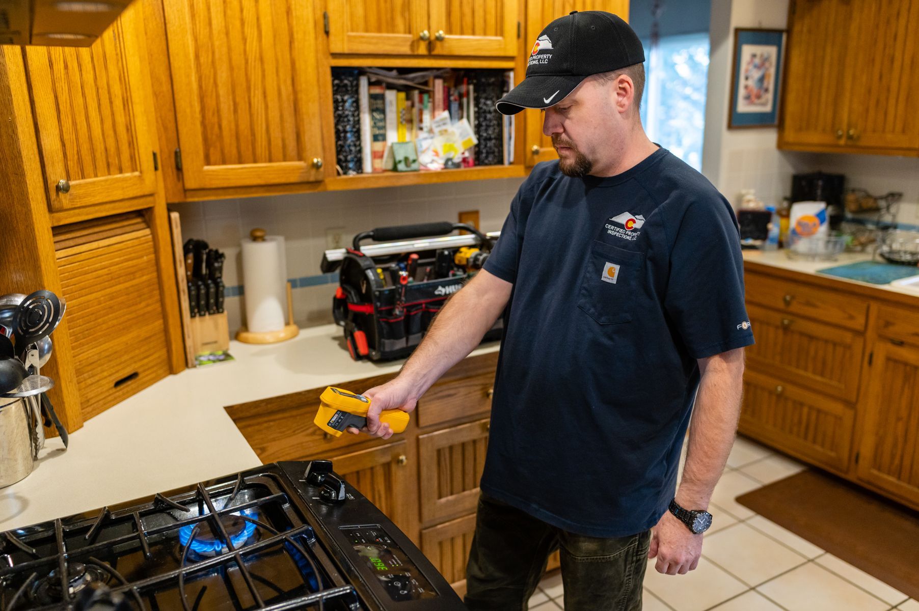 Man in a kitchen holding a yellow tool near a gas stove