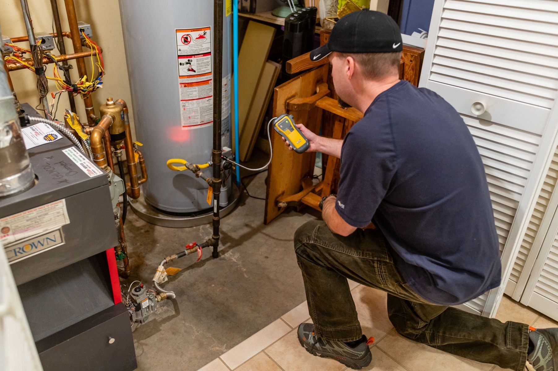 Technician kneels beside a boiler, using a handheld meter in a utility room.