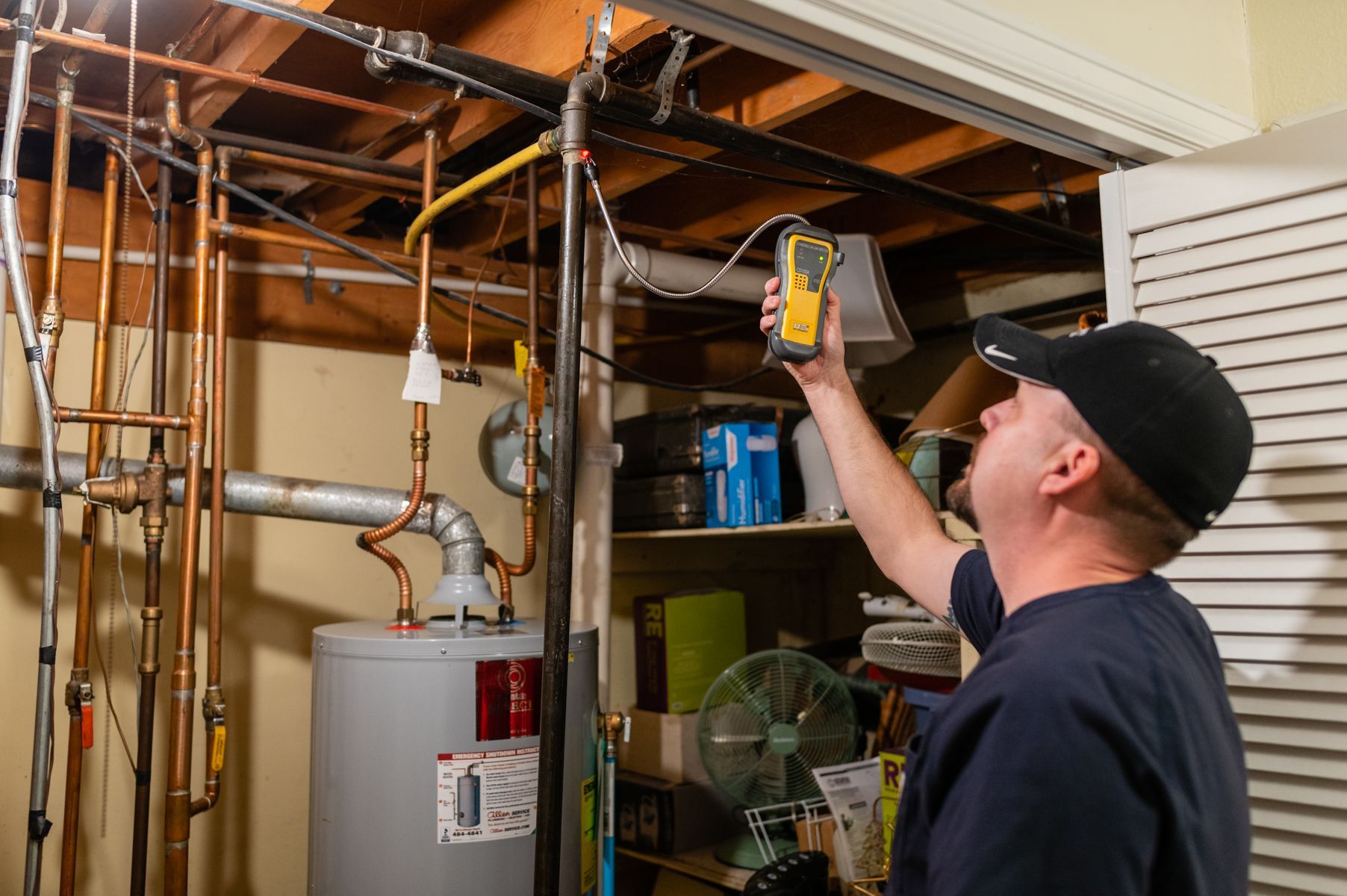 Technician inspecting exposed pipes and electrical wiring in a basement utility room