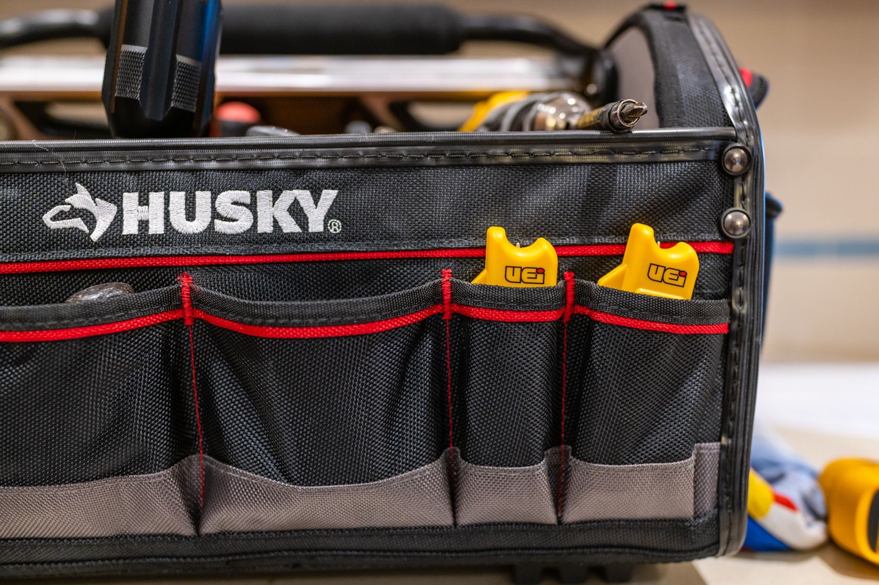Husky tool bag with red-trimmed pockets and yellow tape measures inside