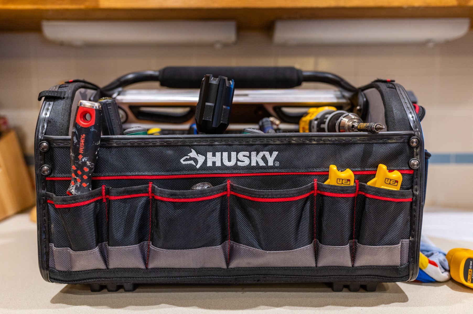 Black Husky tool bag with red accents, filled with hand tools and standing on a shelf
