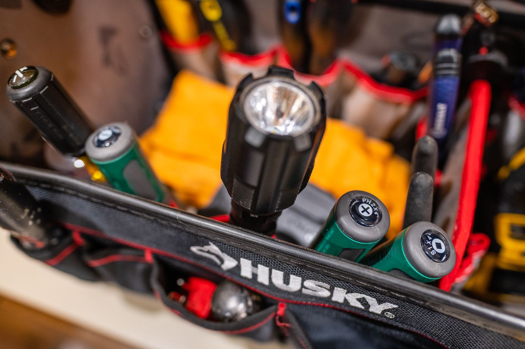 Close-up of a Husky tool bag with flashlights, batteries, and red-handled tools inside