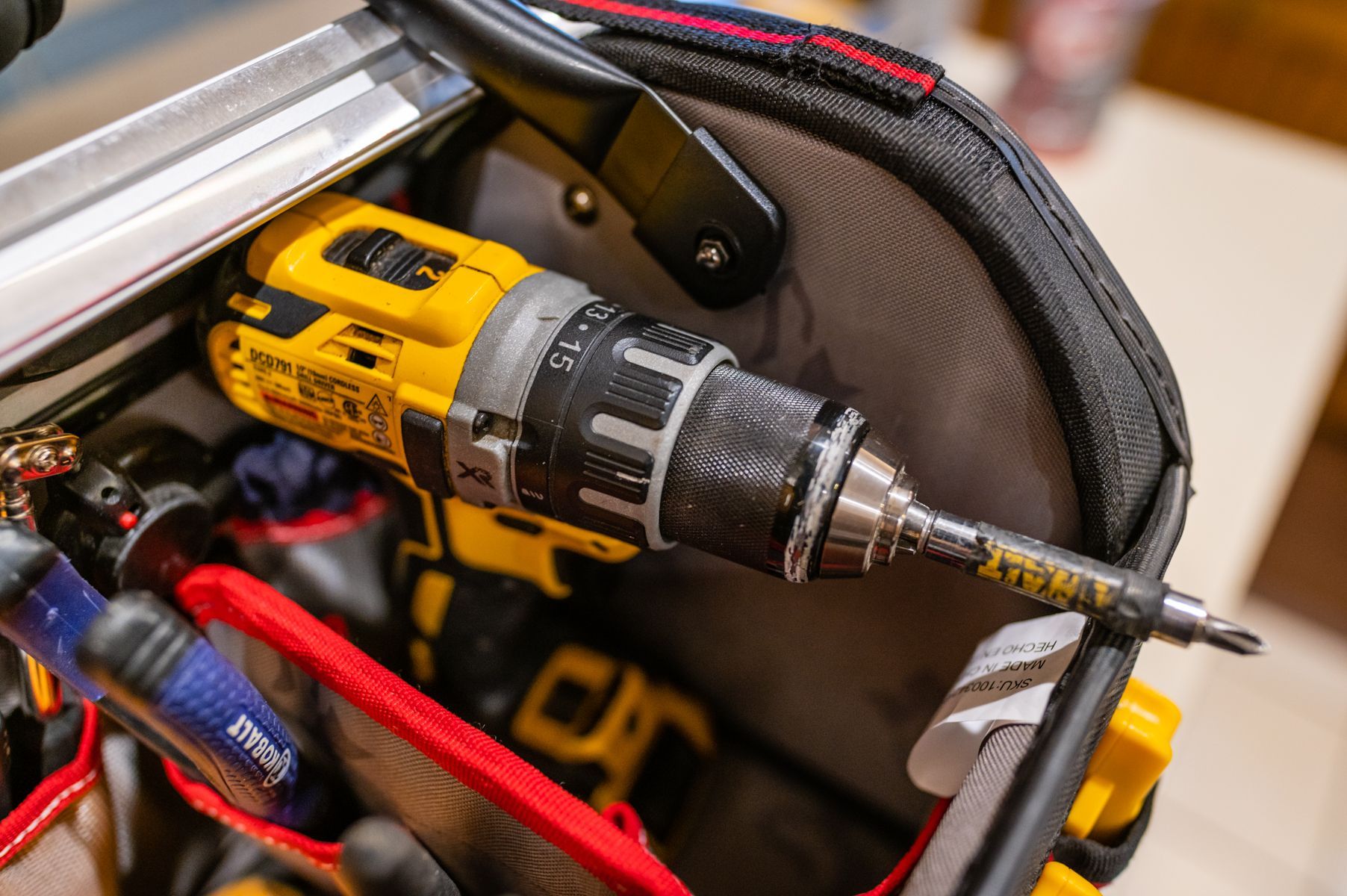 Yellow cordless drill in a tool bag with red and black cables and bits