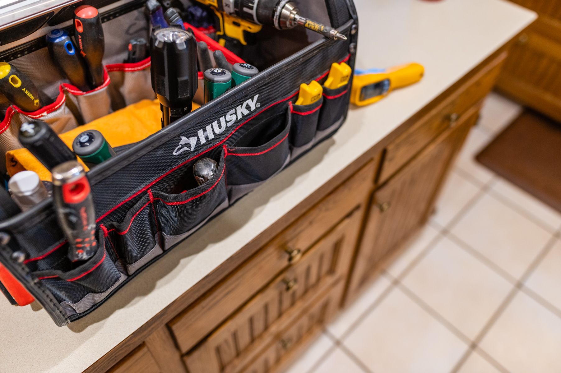 Husky tool bag with hand tools on a wooden cabinet in a tiled workspace
