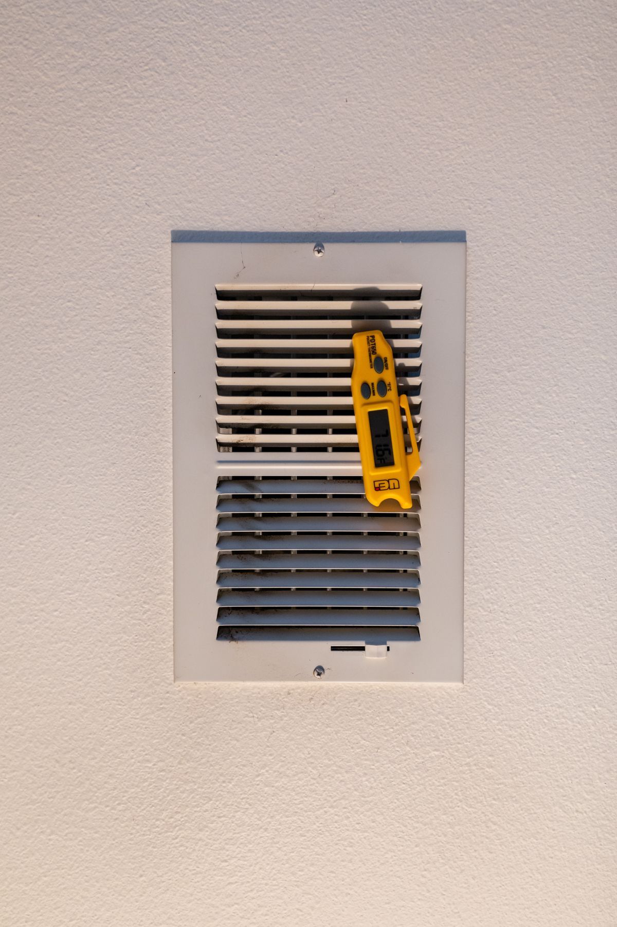 Wall vent with white slats and a yellow utility knife clipped to the right side