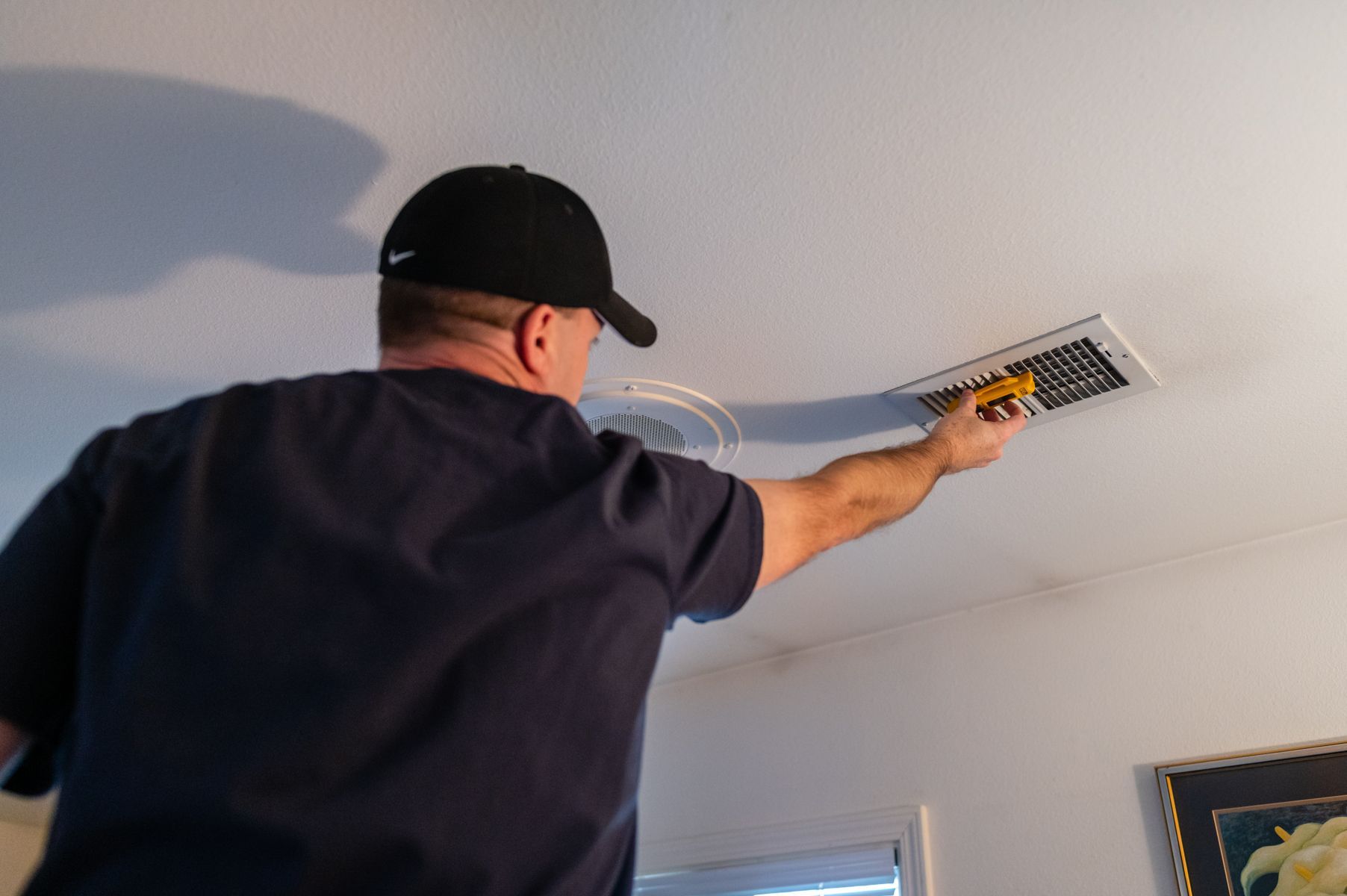 Worker using a yellow tool to inspect a ceiling vent in a room
