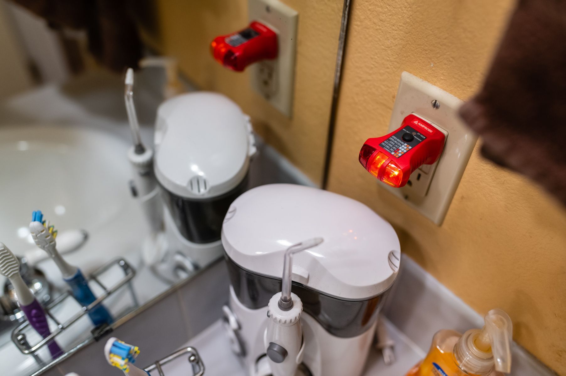 Bathroom sink with soap dispenser and two red-lit wall sensors near the mirror