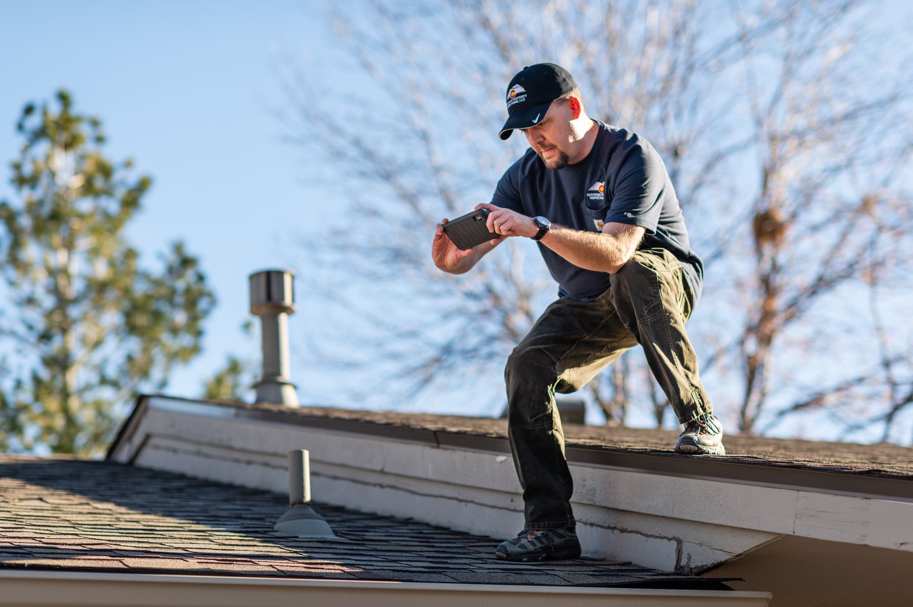 Worker kneeling on a rooftop, using a tool near a chimney on a clear day.