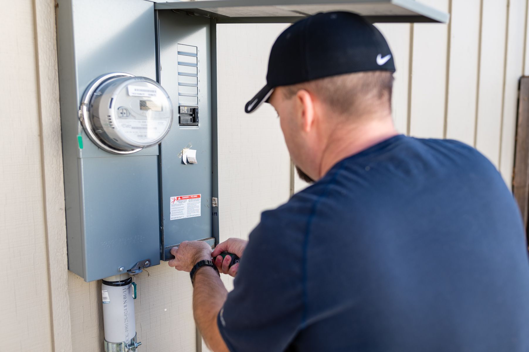 Technician working on an outdoor electrical meter beside a house wall