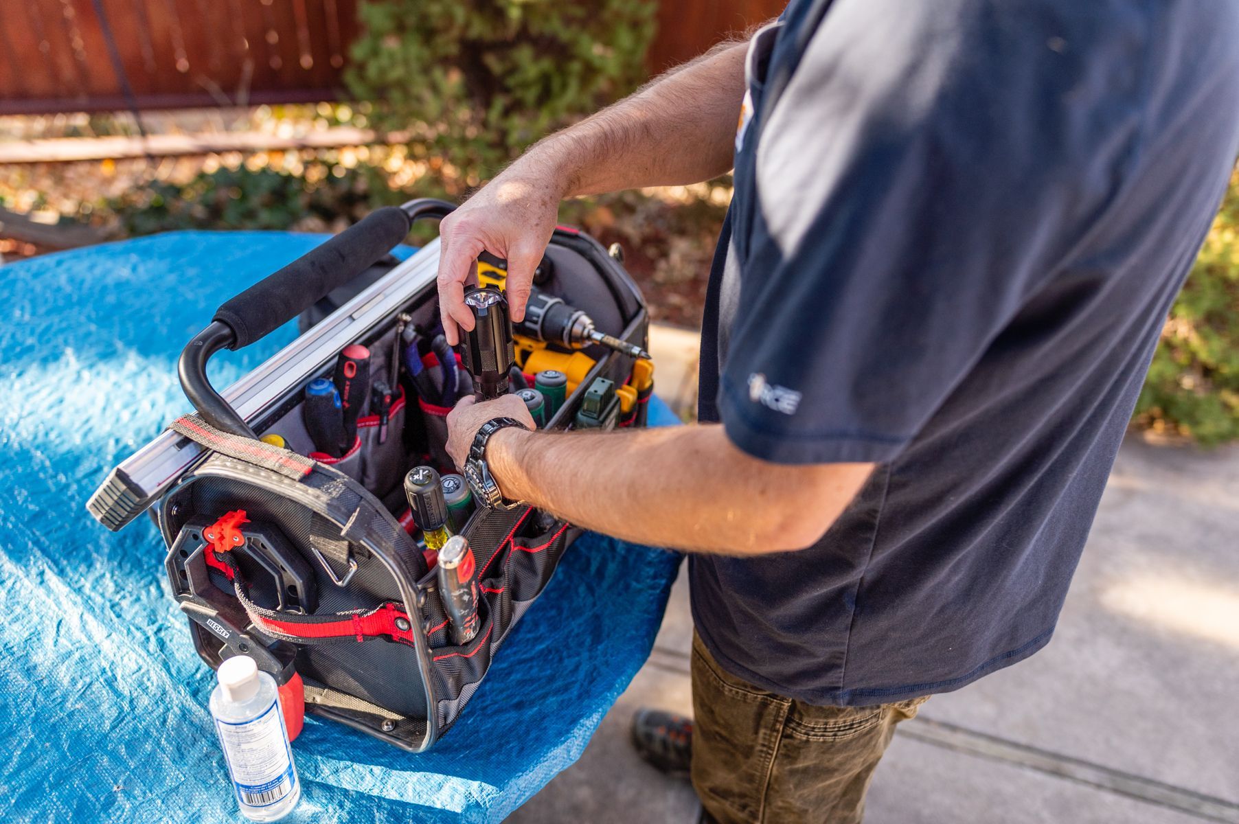 Person working on equipment in a blue bin outdoors, using tools near a sidewalk