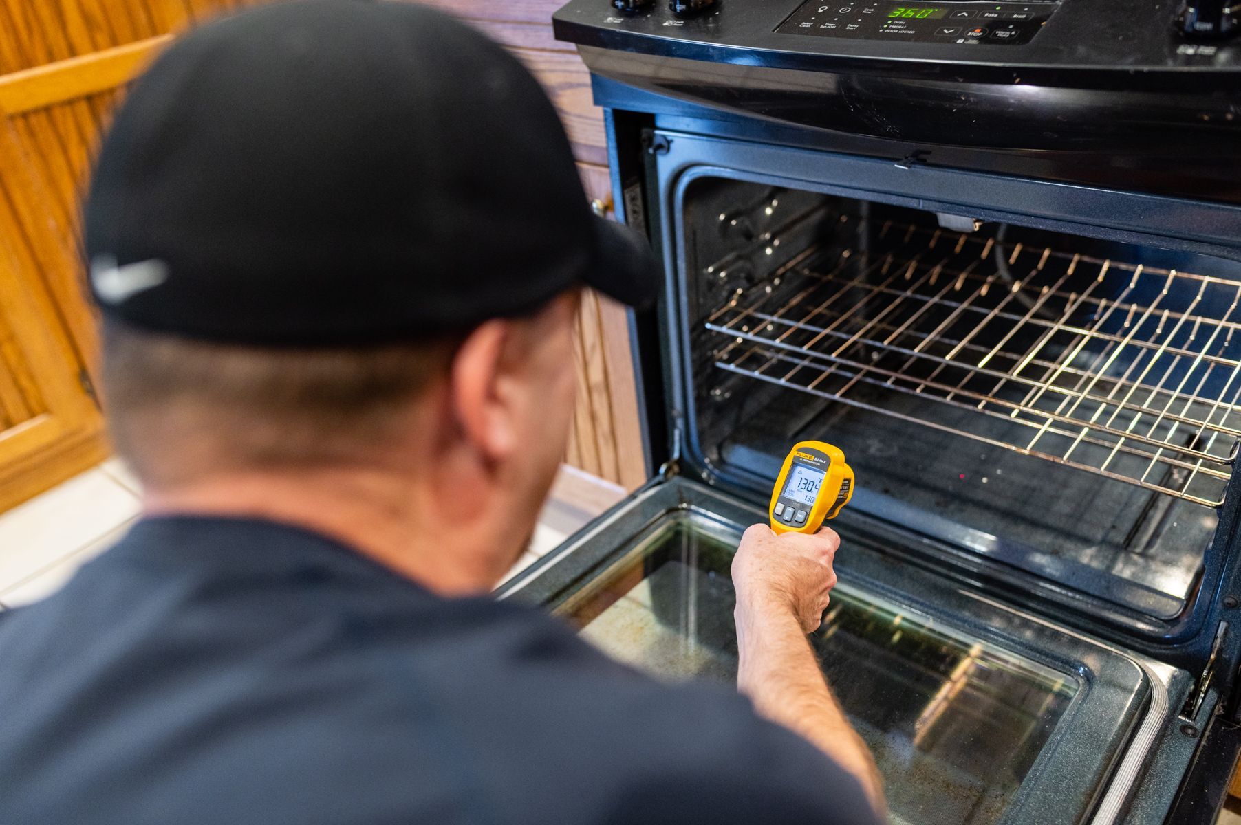 Person measuring the temperature inside an open oven with a handheld thermometer