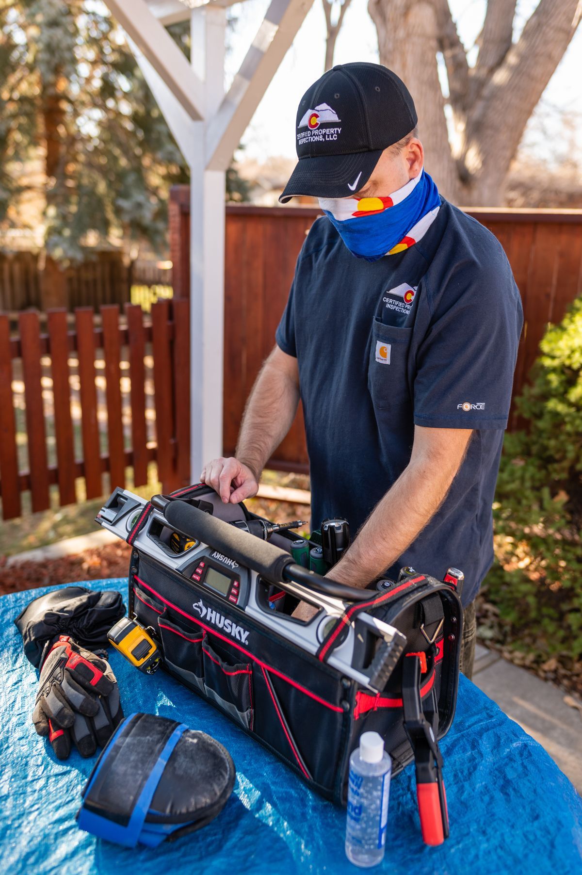 Technician in black shirt and cap adjusting tools on a workbench under a blue tarp outdoors