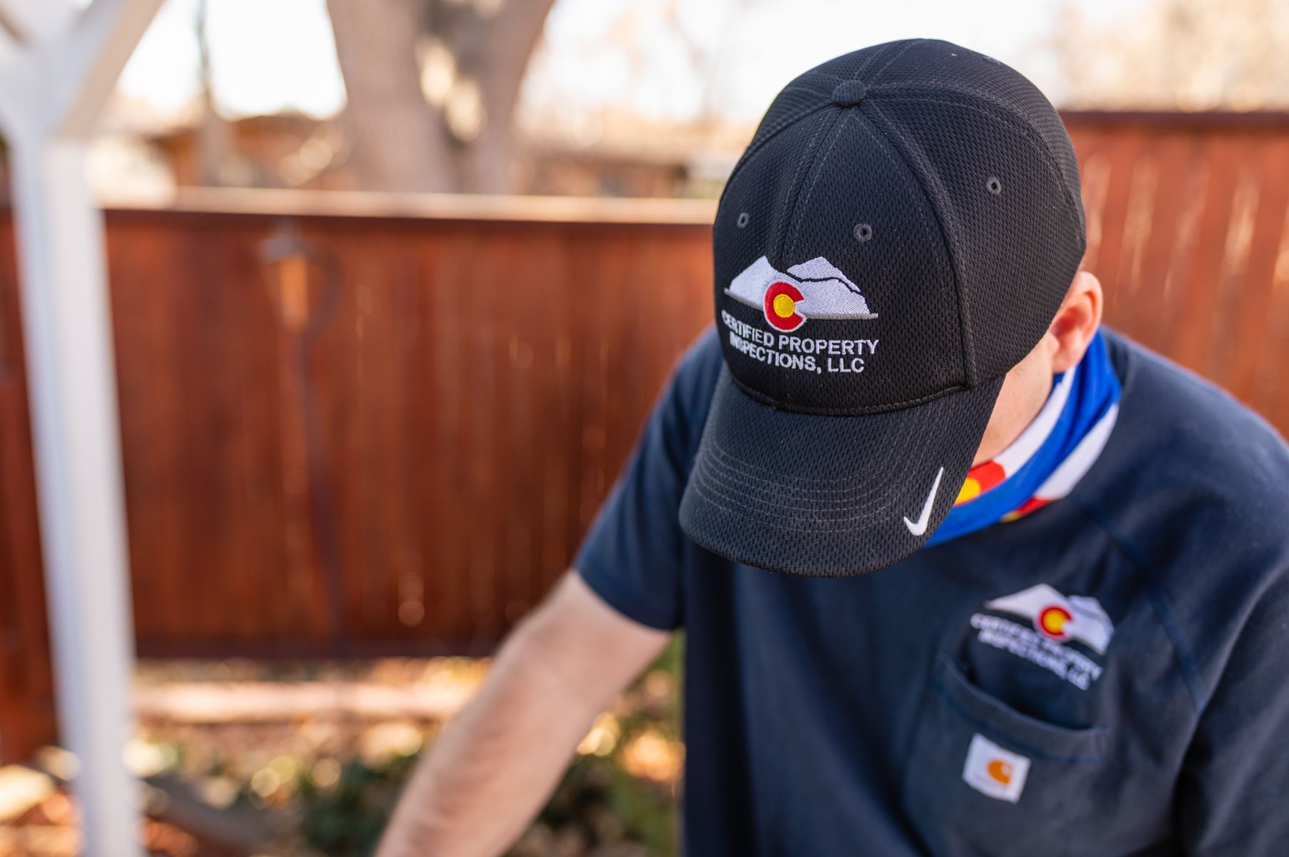 Person in a black cap and navy shirt working outdoors near a wooden fence.