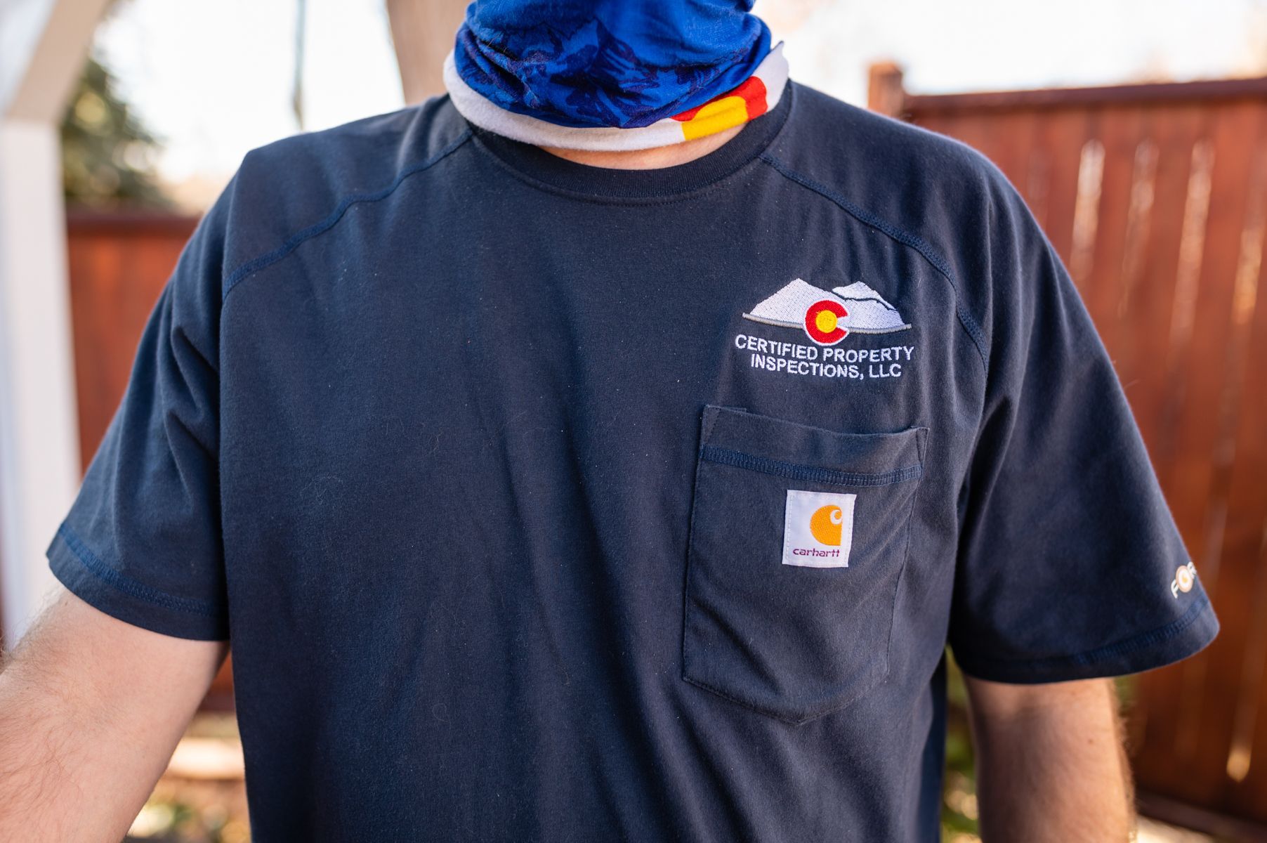 Person in a navy T-shirt with a small logo, standing outdoors with a blue neck gaiter.