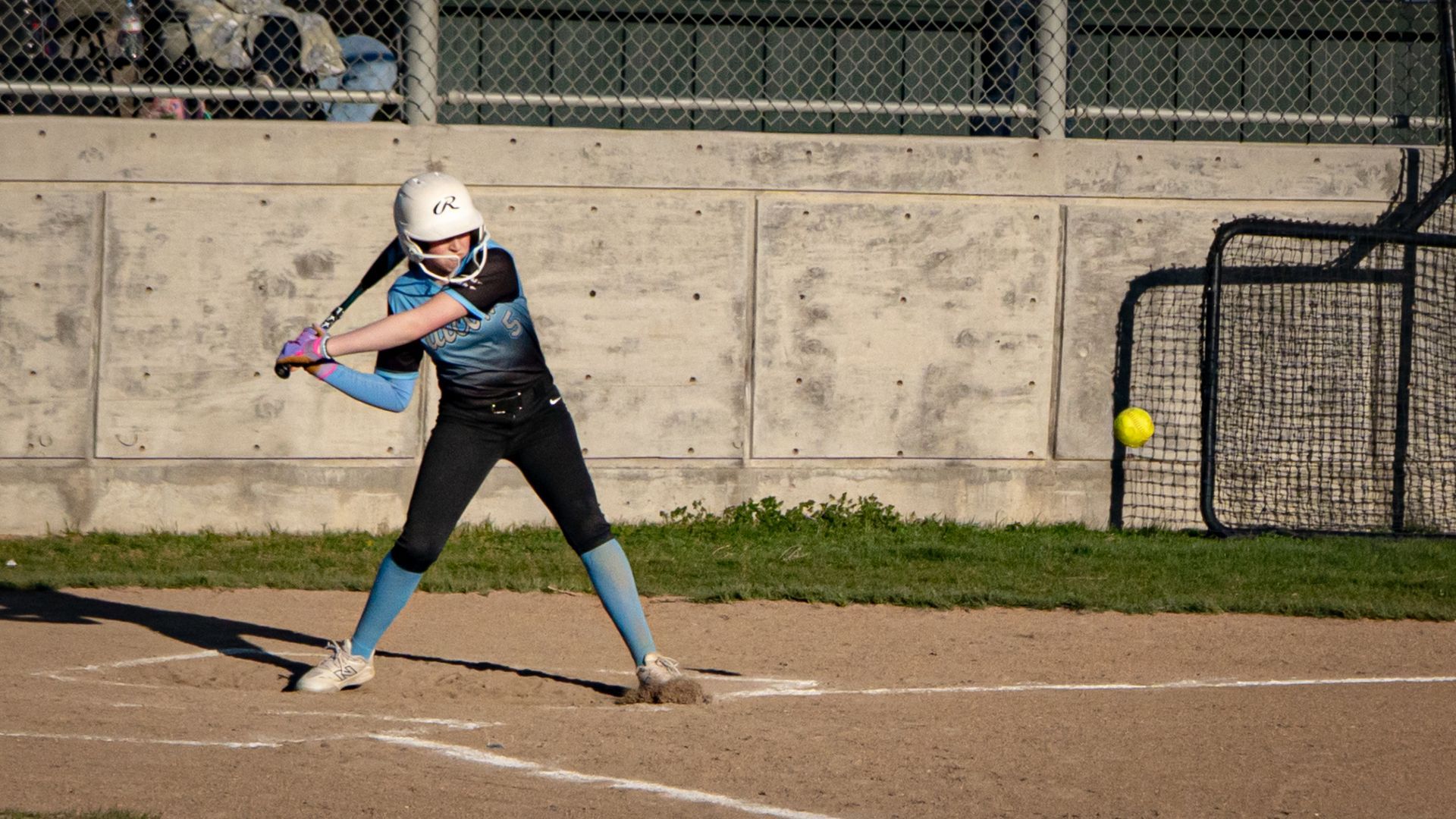 Softball player in uniform at bat, ready to hit.