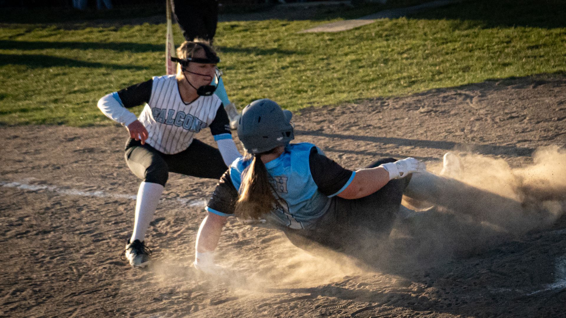 Baseball player sliding into home plate as a catcher tags him amid a cloud of dust