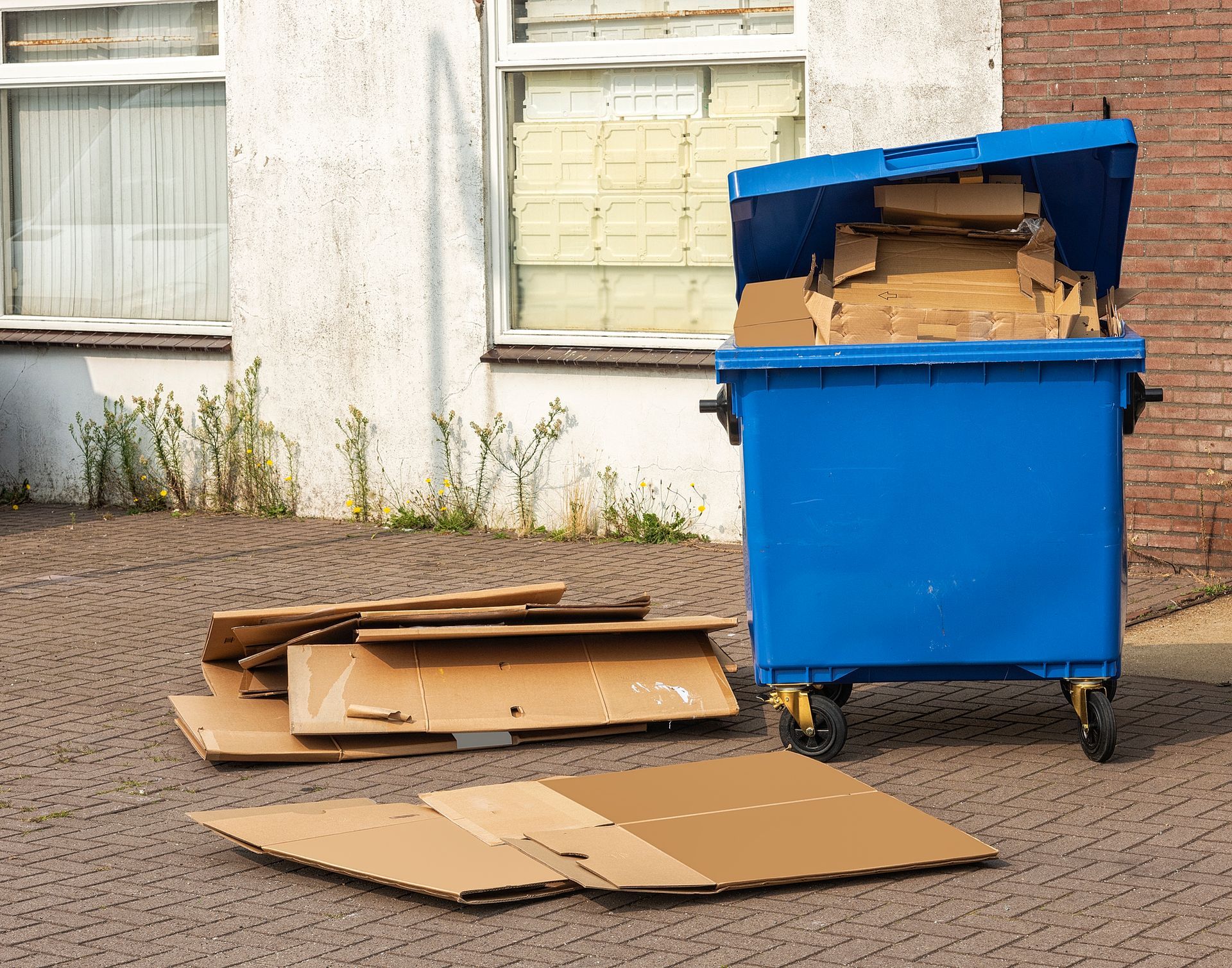 A blue dumpster is filled with cardboard boxes in front of a house.