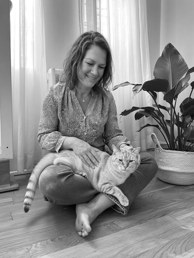 A woman is sitting on the floor petting a cat.