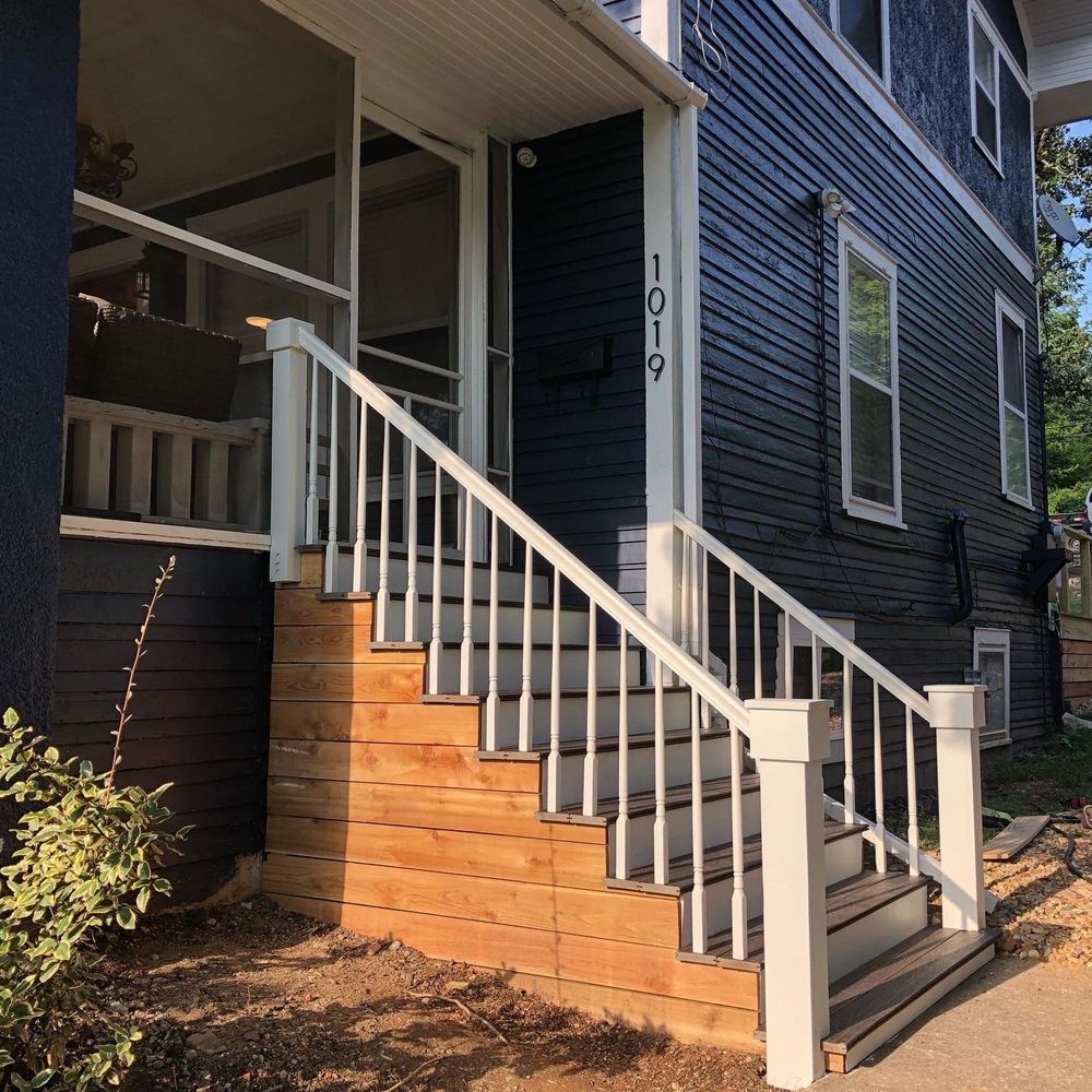 Exterior of a dark blue two-story house with a wooden staircase and white railing leading to the entrance. The house number is 1019.