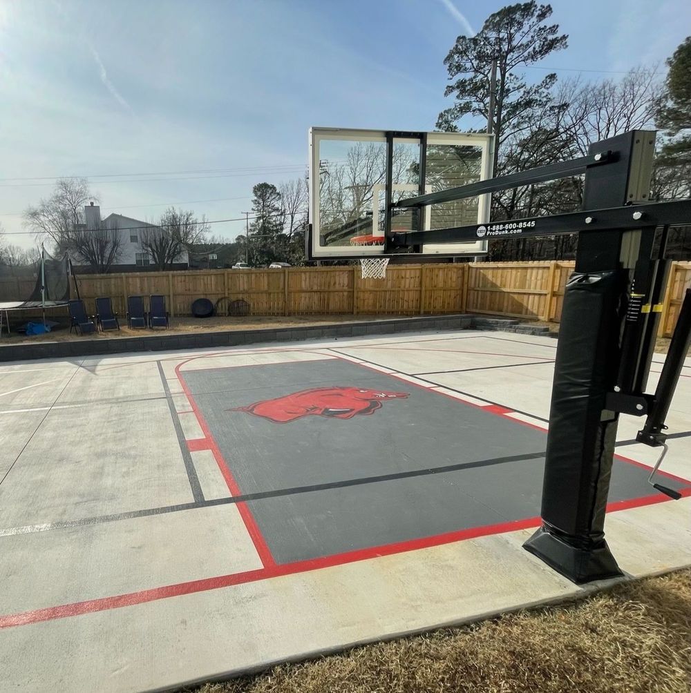 Outdoor basketball court with a gray and red painted surface, hoop, and black pole.