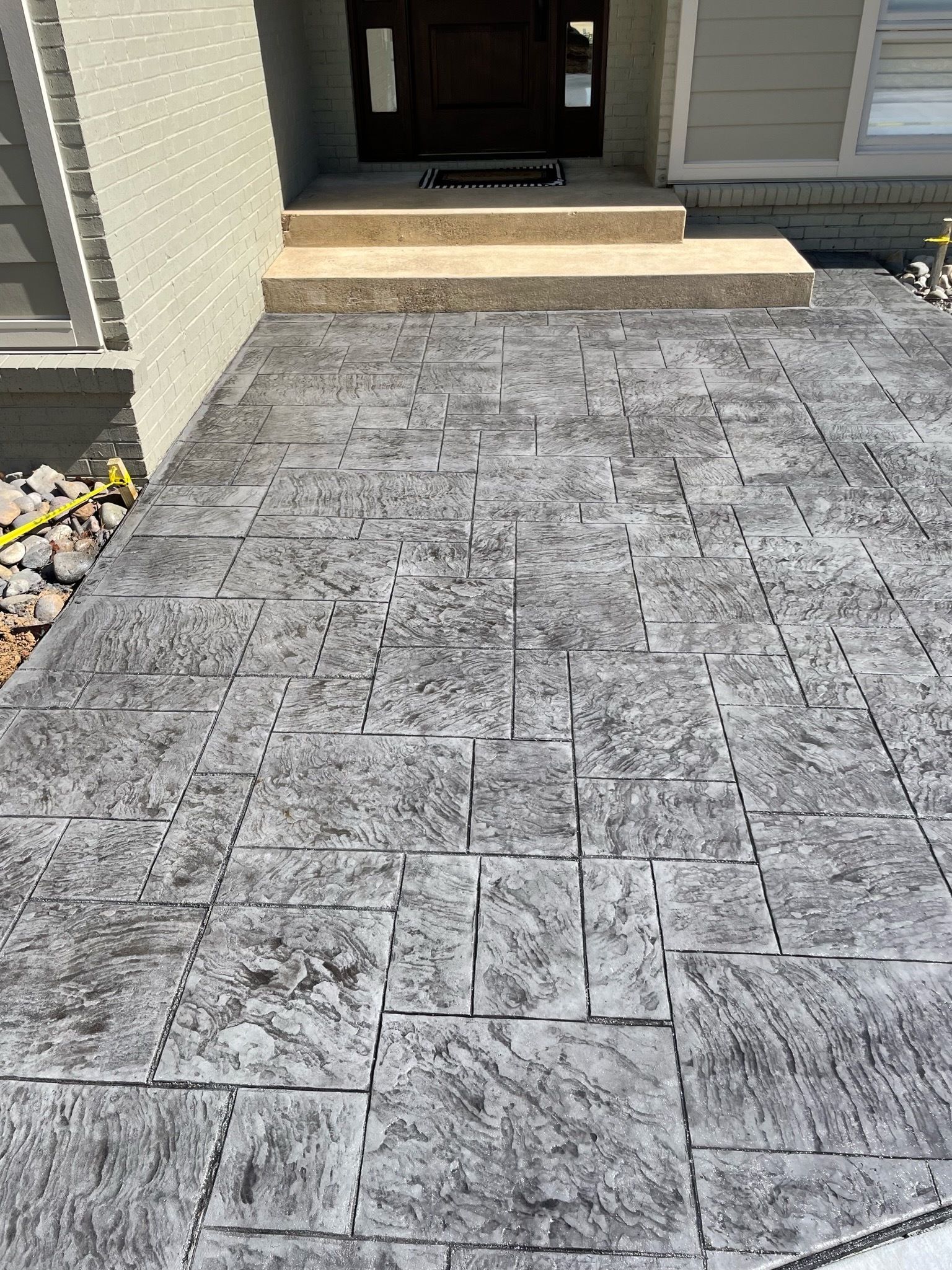 Concrete walkway with textured grey pattern leading to a home's entrance.