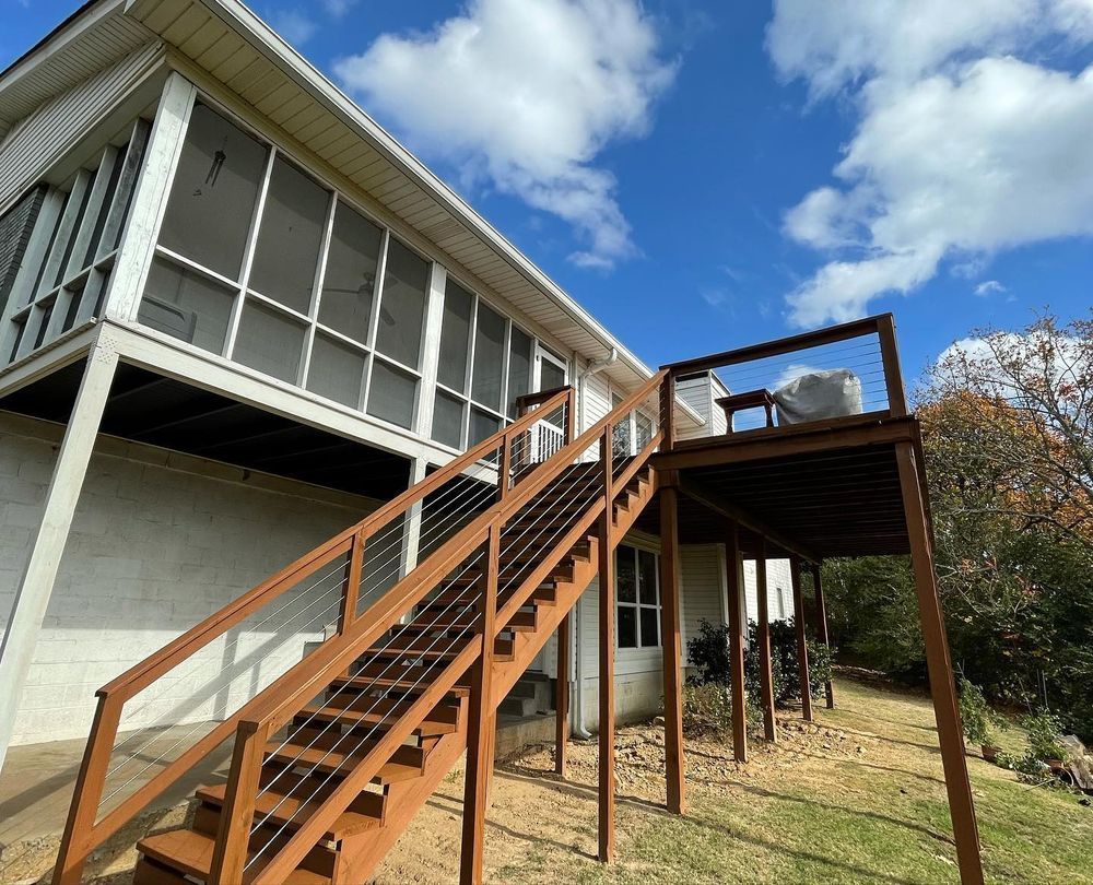 Brown deck with stairs leading up to a screened porch on a white house under a blue sky.