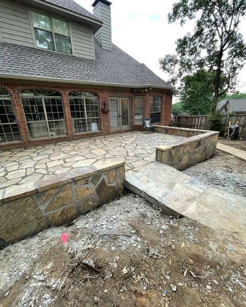 Stone patio with brick house, retaining walls, and pathway under construction.