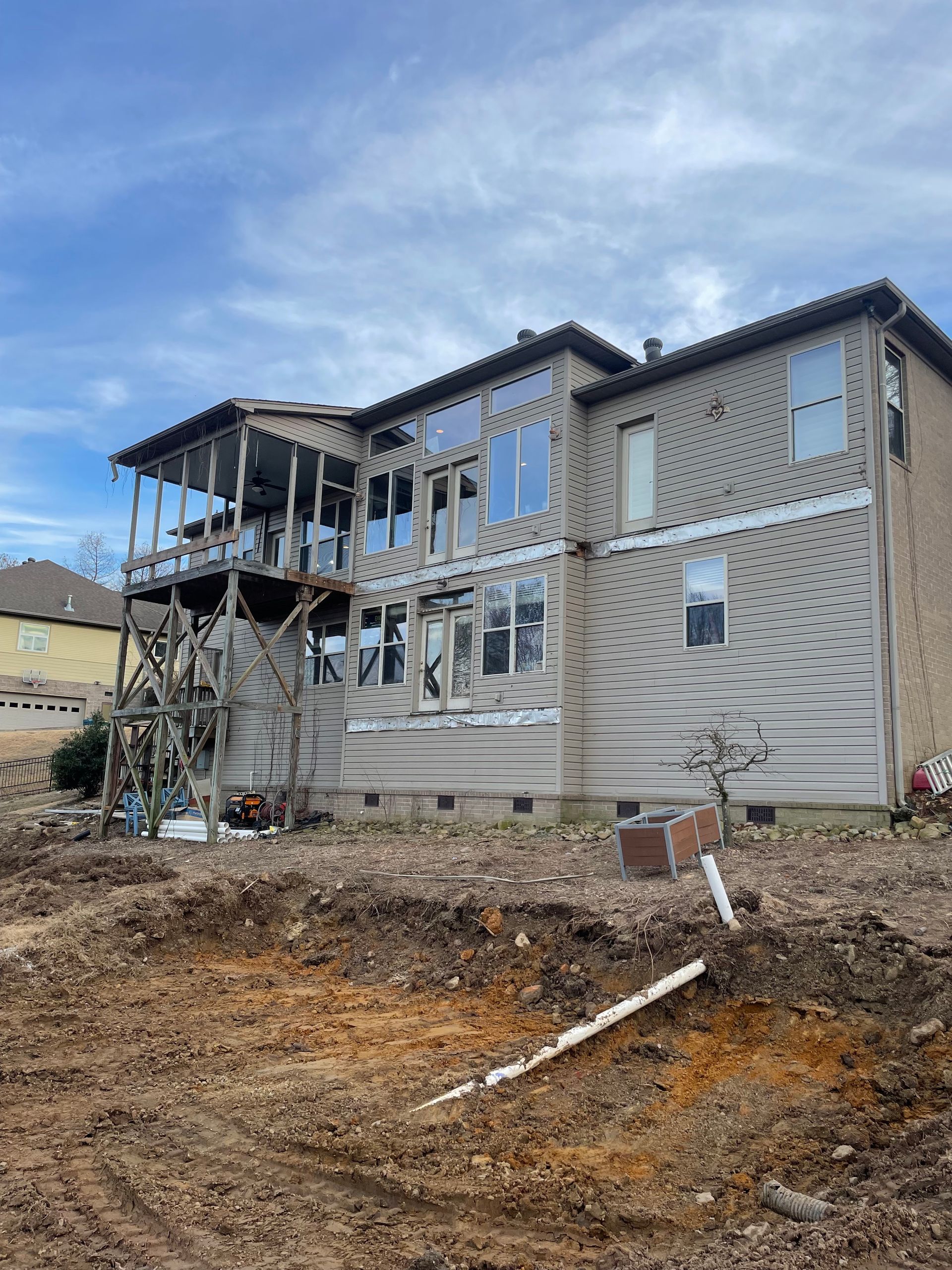 A two-story house with a wooden deck under construction. Beige siding, multiple windows, and a cloudy sky are visible.