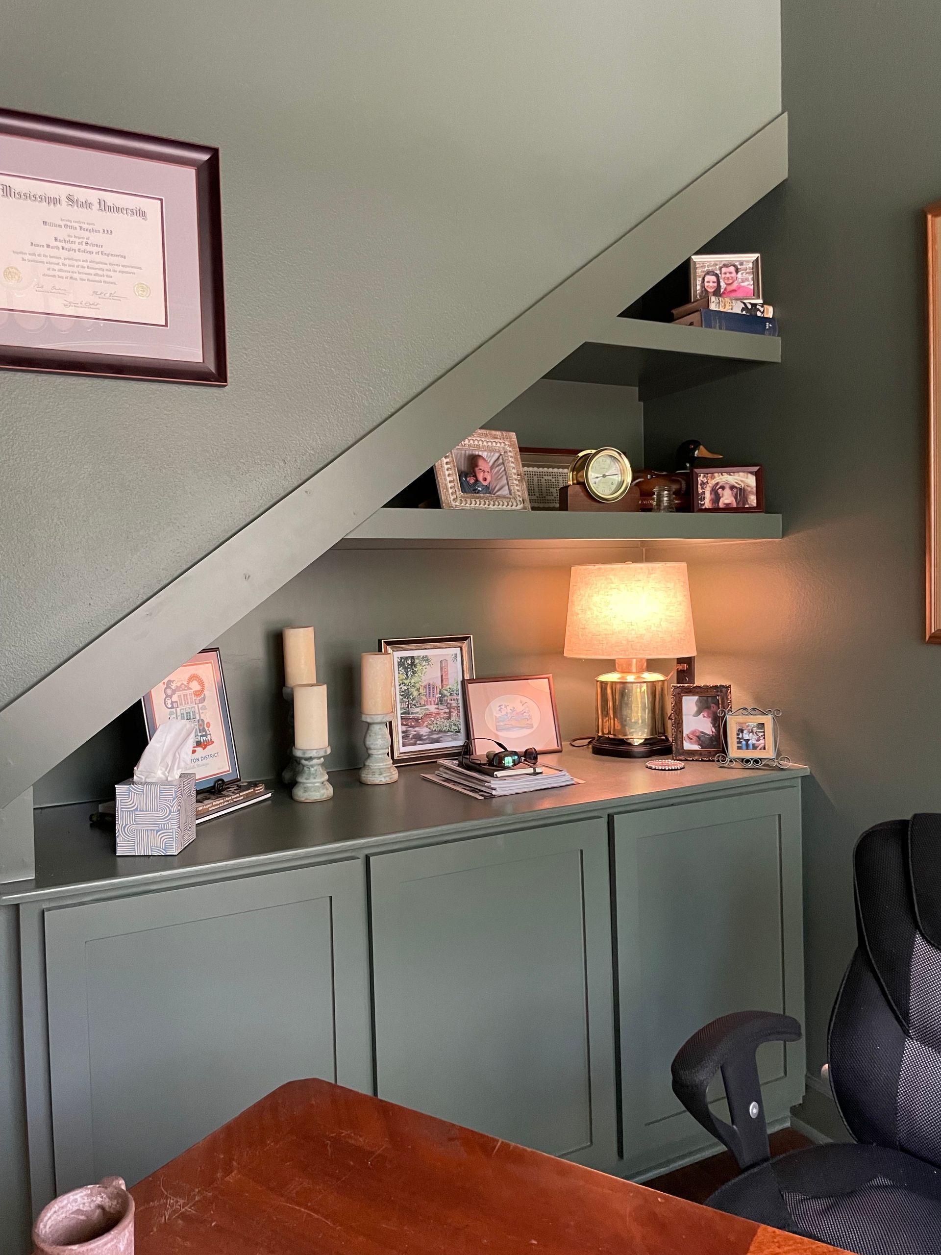 Built-in shelves and cabinets painted green. A lamp and framed photos sit on the surface, beneath the sloping ceiling.