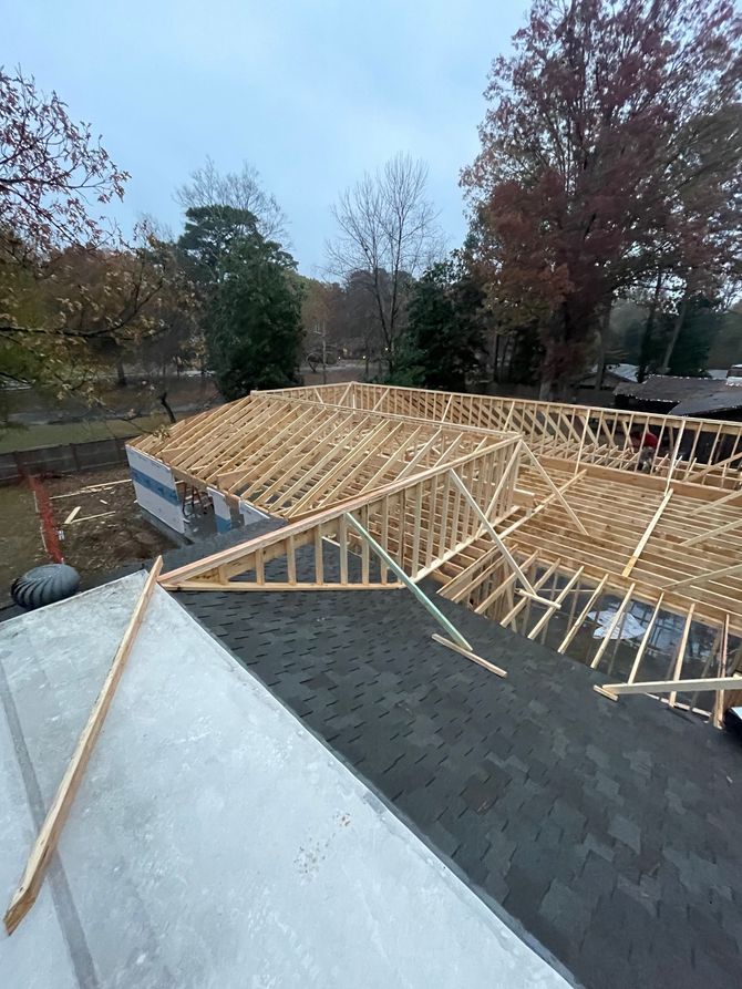 Partially built wooden roof trusses on a house foundation in a wooded area